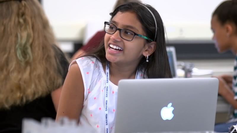 A student smiles in class from behind her laptop.