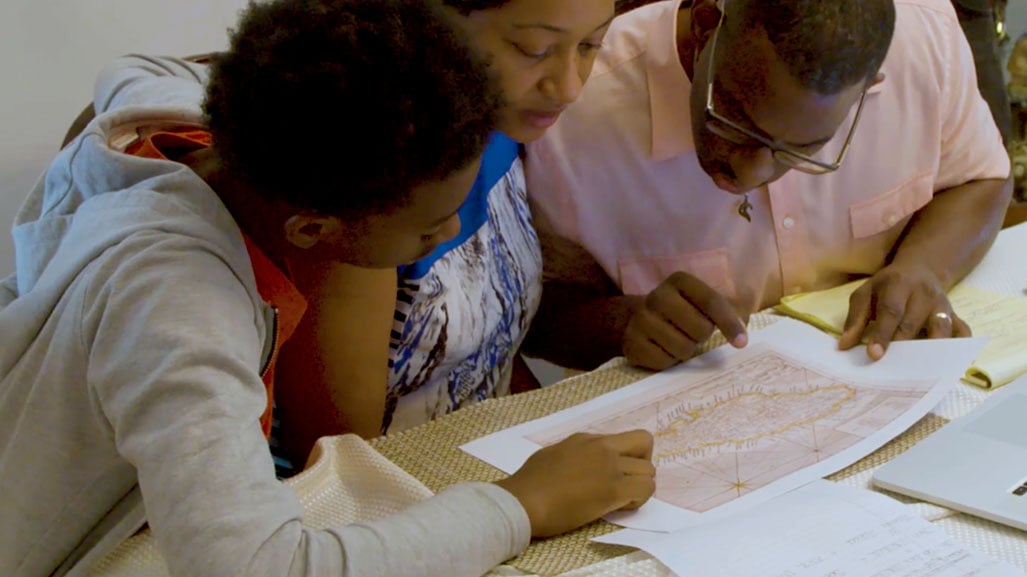 A family of three studies a map on their kitchen table.