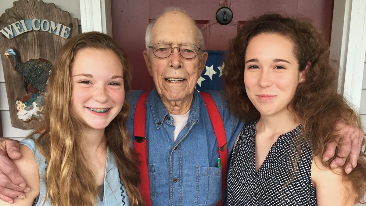 Grandfather poses with his arms around his two granddaughters.